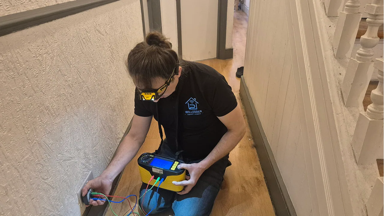 Electrical testing of an indoor socket circuit with EICR test equipment in a hallway.