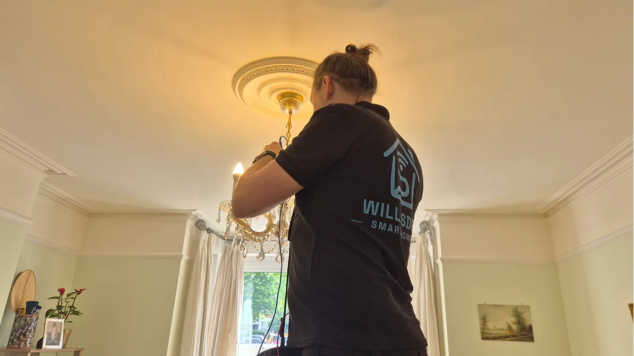 Electrician adjusting a chandelier-style ceiling light in a living room.