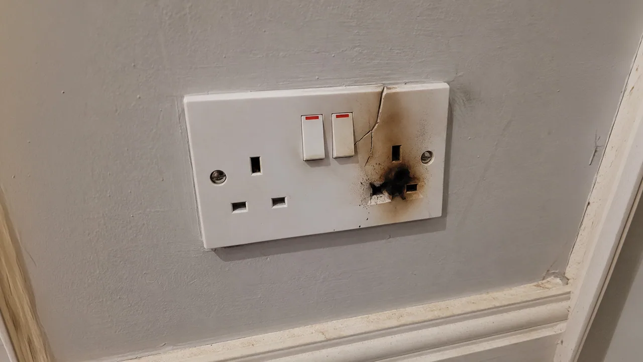 Scorched double socket with heat damage around one switch on a painted wall.