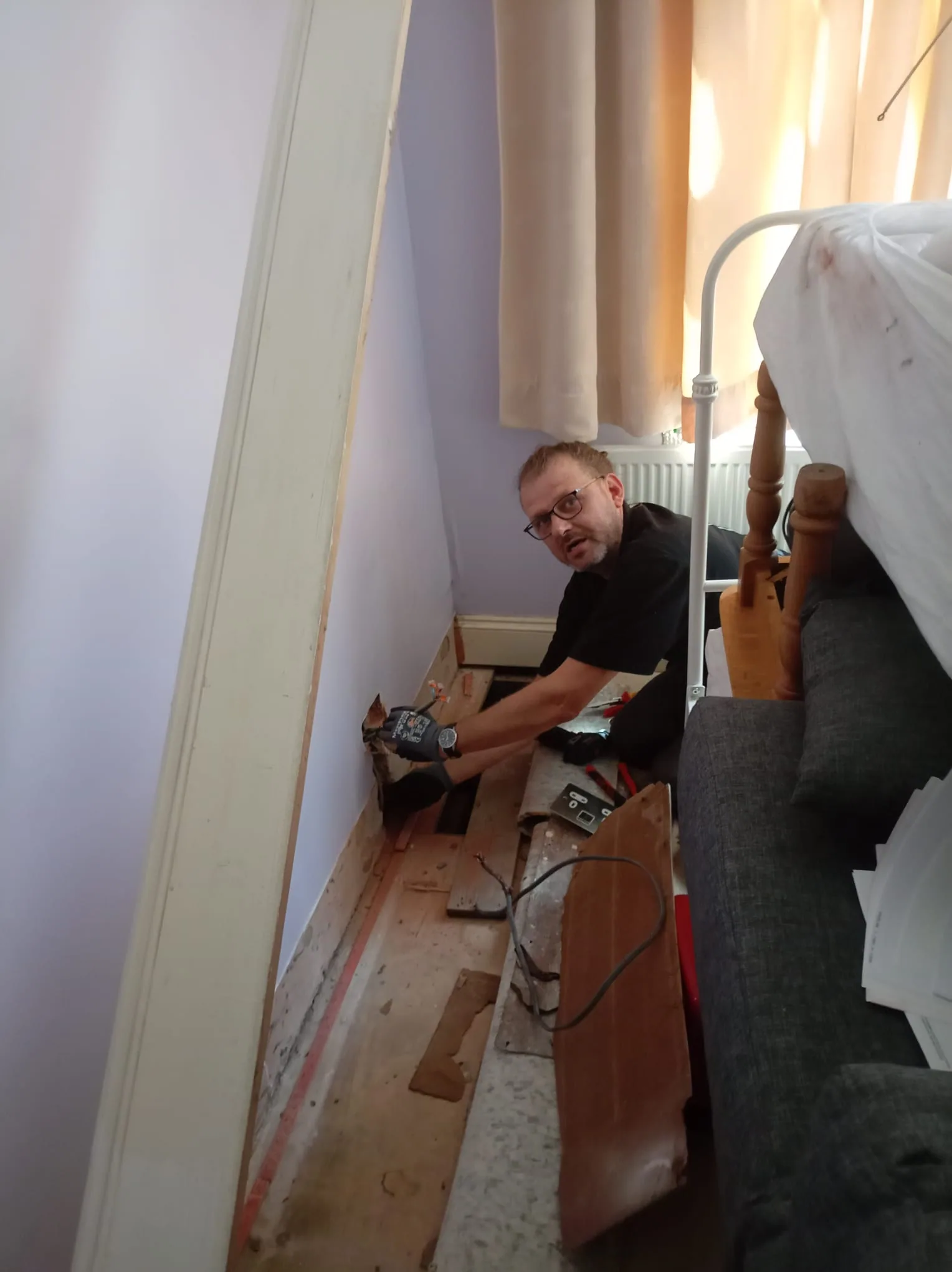 Electrician rewiring beside lifted floorboards in an occupied Victorian bedroom