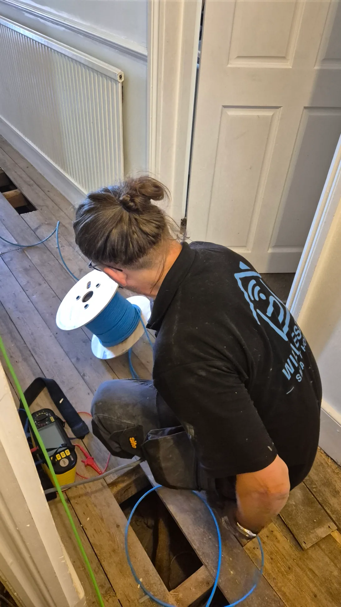 Electrician routing blue cable beneath lifted floorboards in a Victorian house