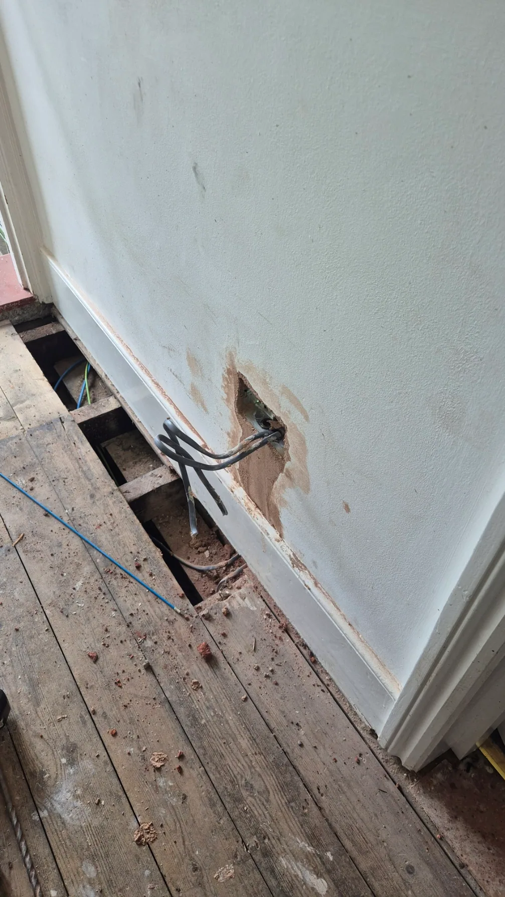 Cables routed through a wall opening above lifted floorboards during a Victorian house rewire