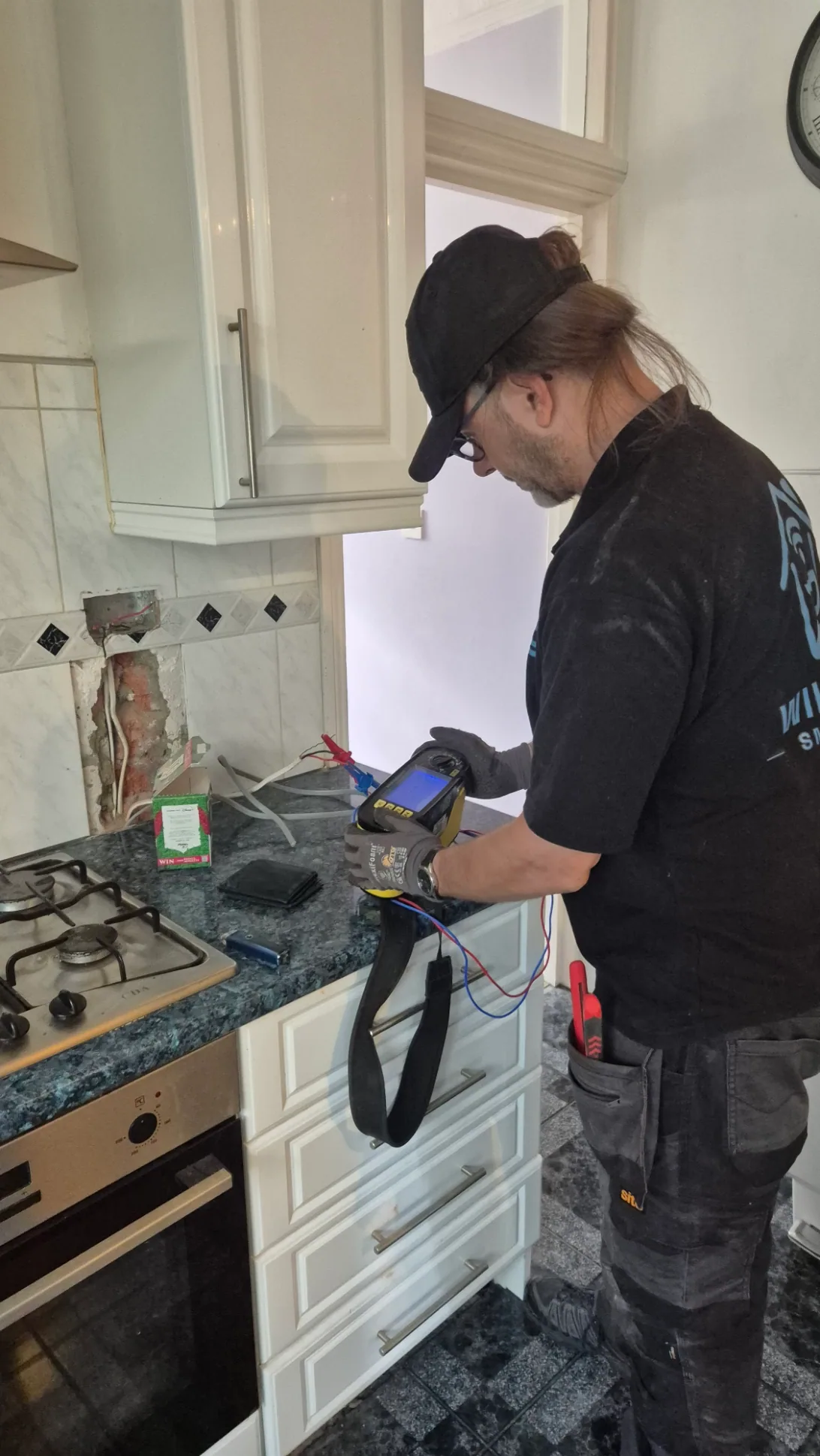 Electrician carrying out electrical testing beside an open wall channel