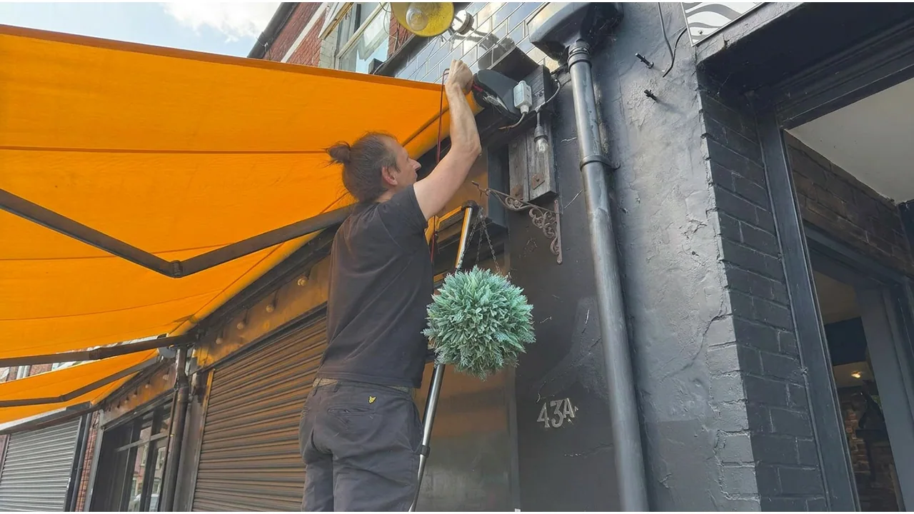 Electrician carrying out electrical work above a shopfront awning.