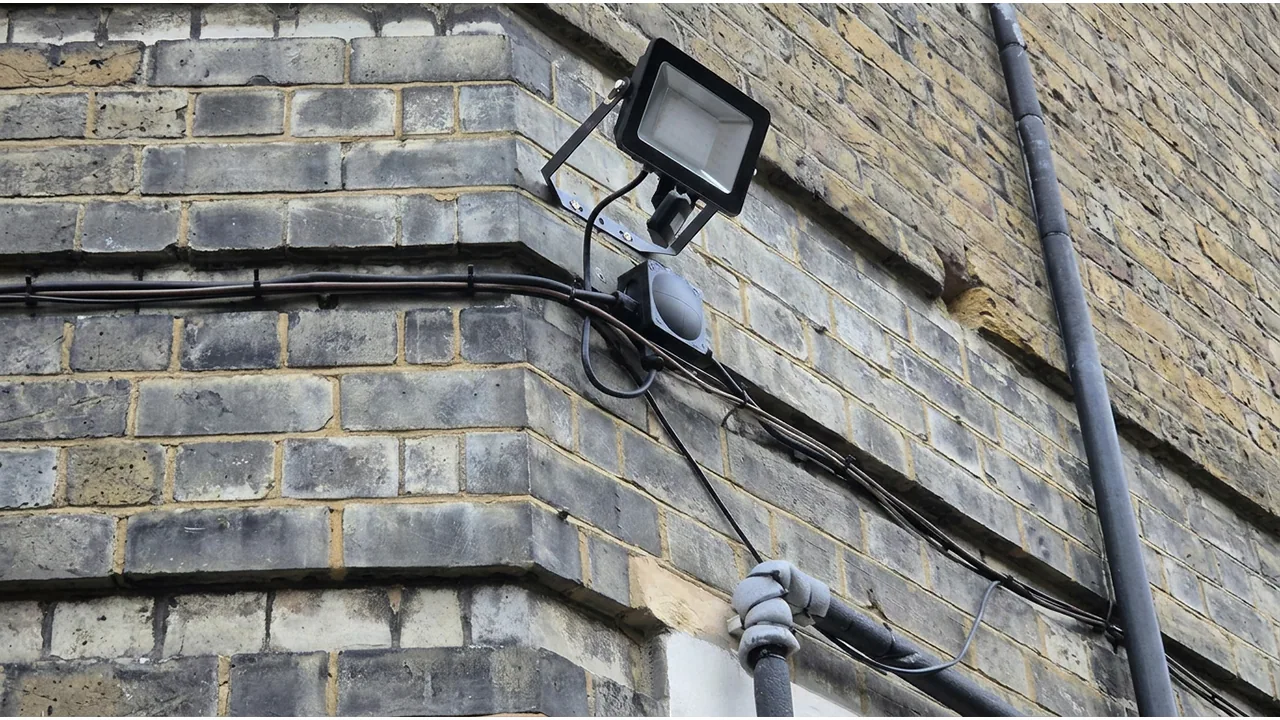 PIR floodlight and surface cabling on a brick corner wall.